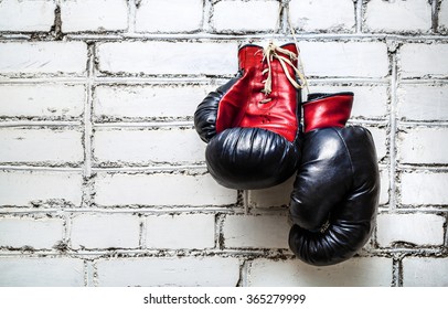 Pair Of Old Red And Black Boxing Gloves Hanging On White Brick Wall.