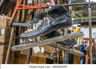 A Pair Of Old Used Worn Out Ice Skates Hanging On A Rod In A Basement Long Forgotten Surrounded By Other Clutter In The Background Indoors