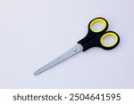 A pair of paper scissors with black handles. Scissors are hand-operated shearing tools. Scissors are used for cutting various thin materials, such as paper, cardboard, metal foil, cloth, rope, and wir