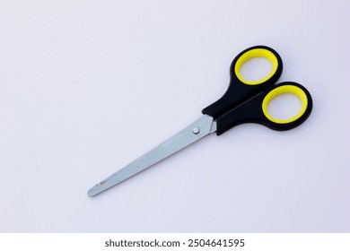 A pair of paper scissors with black handles. Scissors are hand-operated shearing tools. Scissors are used for cutting various thin materials, such as paper, cardboard, metal foil, cloth, rope, and wir