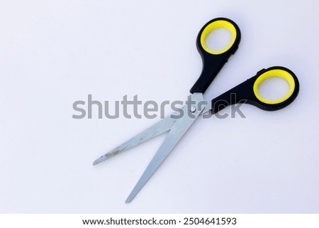 A pair of paper scissors with black handles. Scissors are hand-operated shearing tools. Scissors are used for cutting various thin materials, such as paper, cardboard, metal foil, cloth, rope, and wir