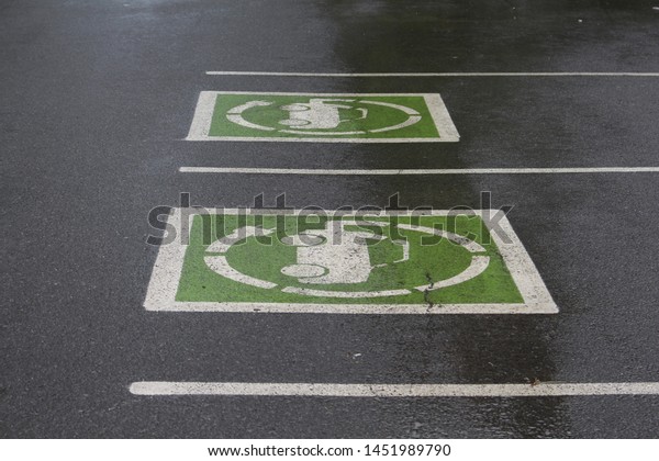 A pair of parking\
spots feature green iconography indicating that they are meant for\
parking and charging electric cars. The parking lot is wet and\
darkened from the rain.