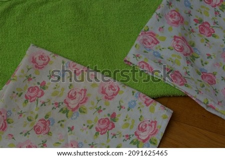 A pair of patterned teatowels lie folded upon a green towel