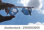 A pair of photochromic glasses is captured against a cloudy blue sky.