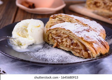Pair pieces of delicious strudel stuffed with apples and cinnamon at a plate next to ice cream ball