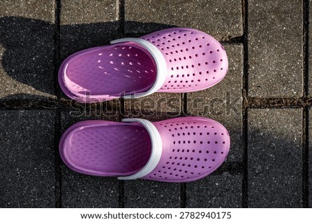 Pair of pink rubber clogs placed on paved stone surface. Casual footwear concept with top view composition.
