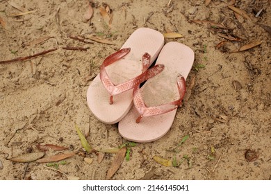 Pair of pink rubber footwear sitting on the ground of a sandy path near the beach, in Australia known as thongs