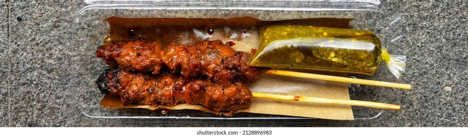 A Pair Of Pork Skewer With Green Chilli Sauce On A Plastic Box Served On Grey Rough Stone Texture Background