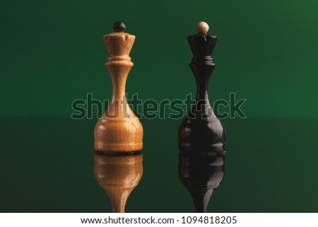 Pair of queen chess pieces confronted as opposites on green background with reflection. Forbidden love, rival figures, copy space
