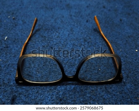 A pair of rectangular glasses placed on a textured blue carpet. The frame has black rims with wood-like temples, creating a blend of modern and natural design.