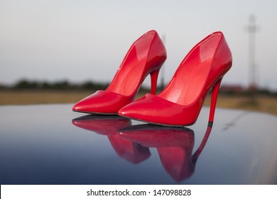 A Pair Of Red High Heel Shoes On Top Of A Blue Car With Reflection