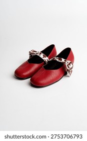 Pair of red leather shoes with patterned strap and buckle isolated on white background.