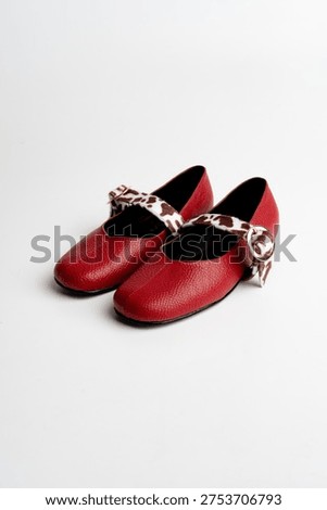 Pair of red leather shoes with patterned strap and buckle isolated on white background.
