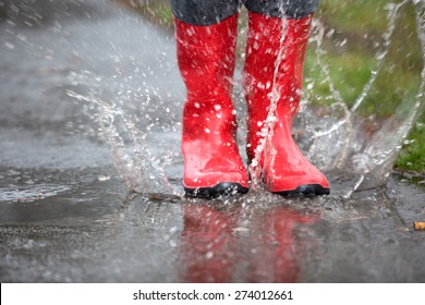 A pair of red rubber boots are jumping into a big puddle.