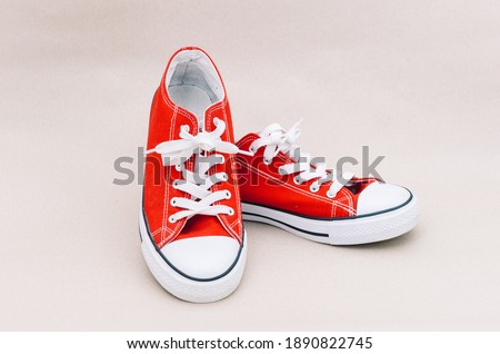 Pair of red, unisex, vintage, grunge style sneakers (gumshoes) placed in the plain isolated color background. Sneakers made out of red fabric with white laces, white rubber soles and accessories.