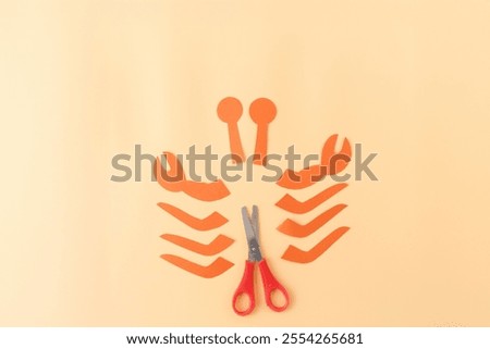 a pair of red-handled scissors and several pieces of orange paper cut into various shapes. what appear to be crab claws, legs, materials for a craft project, DIY project 