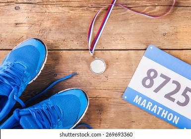 Pair Of Running Shoes, Medal And Race Number On A Wooden Floor Background