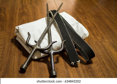 A Pair Of Sai (traditional Okinawa Kenpo Karate's Weapon), Black Belt (Karate, Judo, Kenpo, Jiu-Jitsu, Budo, Martial Arts, Taekwondo) And Gi (Japanese Martial Arts Uniform) On The Wood Floor