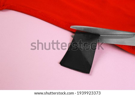 A pair of scissors cutting a tag off. Tag trim on baby clothes, close up.Tags that pierce the skin