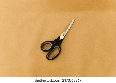 A pair of scissors laying on top of a sheet of brown paper on a flat surface
