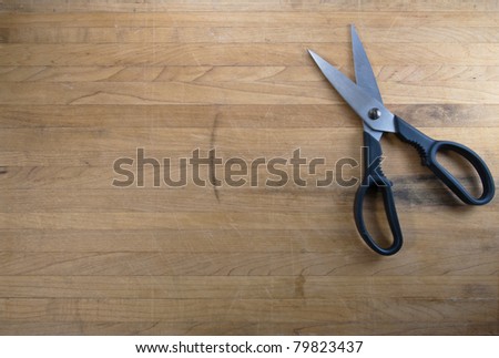 A pair of scissors sits half open on a worn butcher block counter top