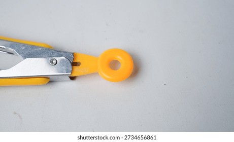A pair of scissors with a yellow handle and a yellow ring. The scissors are open and the ring is on the table