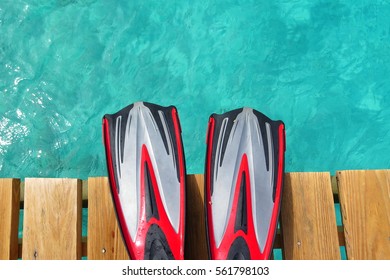 Pair of scuba fins on the pier above the tropical sea. Red fins over the blue water. Tropical paradise close to the sea. Scuba vacation on the tropical island.