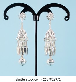 A Pair Of Silver Earrings On Blue Background