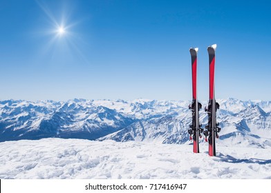 Pair of skis in snow with copy space. Red skis standing in snow with winter mountains in background. Winter holiday vacation and skiing concept. 