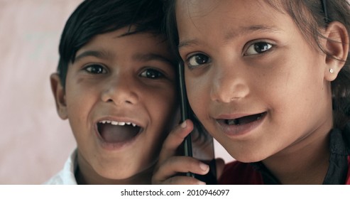 A Pair Of Smiling South Asian Children Talking On A Phone Together