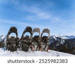 A pair of snowshoes resting in deep snow against a backdrop of mountain ranges. Snowshoeing is popular in regions like the Alps, Rockies, Scandinavia, and the Pyrenees.