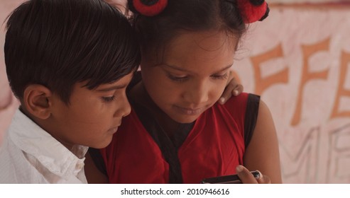 A Pair Of South Asian Children Looking At A Phone Together