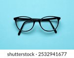 Pair of spectacles eye glasses folded on cyan blue background top view