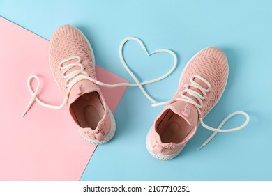 Pair of sportive shoes and heart made of laces on color background