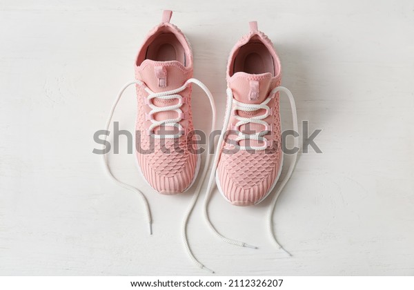 Pair of sportive shoes with untied laces on\
light wooden background