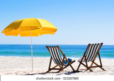 Pair of sun loungers and a beach umbrella on a deserted beach; perfect vacation concept 