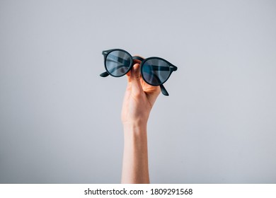 Pair Of Sunglasses Held In Front Of Grey Background Photo - Hands hold up a pair of black sunglasses in front of a clean grey background.

