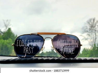  A pair of sunglasses on the car dashboard with a beautiful scenery background with written text forget the past, focus on future. Selective focus.