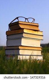 A Pair Of Thick Black Women's Eyeglasses Sit On Top Of A Stack Of Thick Old Books, Bibles, And Hymnals Outside.