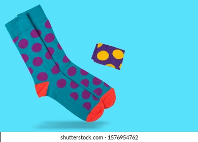 a pair of turquoise socks with lilac peas, on a turquoise background, as if standing at your fingertips, one sock rolled up, as if flying, concept, copy space