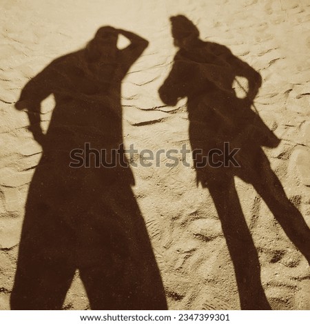 A pair of two black shadows of a man and a young girl on the sand. Shadows of two friends on white fine sand talking to each other. Two figures in the form of dark shadows are surprised and discussing