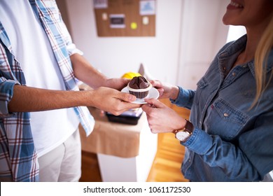 Pair Of Two Young People Sharing A Chocolate Muffin In The Office During A Break.