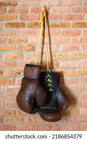 A Pair Of Vintage Boxer Leather Gloves Hang Against A Brick Wall. Retro Style.	A Vertical Image.