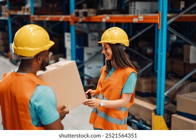 A pair of warehouse employees, dressed in hard hats and safety vests, work together to handle a cardboard box, symbolizing teamwork and collaboration in a well-organized storage facility. - Powered by Shutterstock