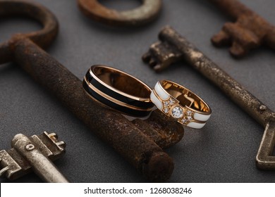 Pair of wedding enamel rings on gray background with vintage rusty keys. Two-tone wedding rings with white and black enamel. Romantic fashion jewelry advertising