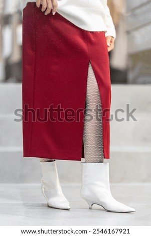Pair of white boots with pointed toe and small heel on legs of woman in red Skirt with slit and white lace tights, low angle, fashion look detail, shoes and clothes