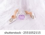 A pair of white bridal shoes, a bottle of perfume against the background of a satin white dress and a veil. The concept of wedding dress. Front view