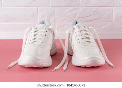 Pair Of White Chunky Sole Sneakers On A Pink Coral Colored Floor. New Female Or Teen Untied Laces Shoes For Active Lifestyle, Fitness And Sports. Front View.