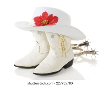 A Pair Of White Cowgirl Boots Topped By A White Hat With A Red Poinsettia With Spurs Laying Nearby.  On A White Background. 