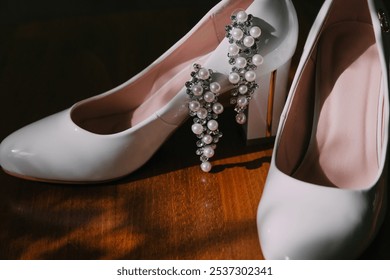 A pair of white shoes with pearls on the toe and heel. The shoes are placed on a wooden surface - Powered by Shutterstock